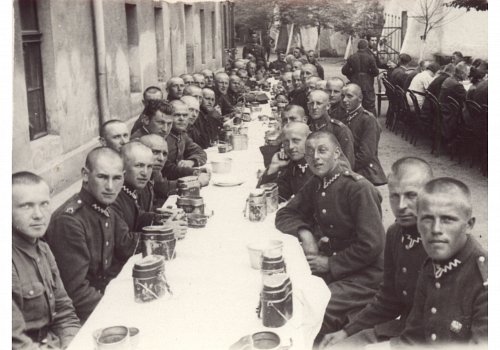 Plik cyfrowy; Pochodzenie: Żory, G&oacute;rny Śląsk; Datowanie: lata 1922-1939; Autor: brak danych 
Fotografia czarno-biała przedstawiająca żołnierzy II Dywizjonu 23 Pułku Artylerii Lekkiej w Żorach podczas wsp&oacute;lnego obiadu na placu koszarowym po przysiędze wojskowej.