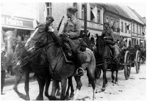 Plik cyfrowy; Pochodzenie: Żory, G&oacute;rny Śląsk; Datowanie: 1922-1939; Autor: brak danych 
Fotografia czarno-biała przedstawiająca żołnierzy II Dywizjonu 23 Pułku Artylerii Lekkiej w Żorach podczas powrotu z letnich manewr&oacute;w. Na pierwszym planie widoczni żołnierze obsługi I działa 5 baterii. W tle zabudowanie jednej z ulic w Żorach.