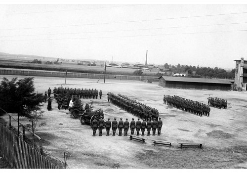 Plik cyfrowy; Pochodzenie: Żory, G&oacute;rny Śląsk; Datowanie: lata 1922-1939; Autor: brak danych 
Fotografia czarno-biała przedstawiająca żołnierzy II Dywizjonu 23 Pułku Artylerii Lekkiej w Żorach w trakcie przysięgi wojskowej. Fotografia wykonana na placu przed zabudowaniami garnizonowymi z ptasiej perspektywy.