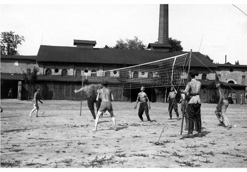 Plik cyfrowy; Pochodzenie: Żory, G&oacute;rny Śląsk; Datowanie: lata 1922-1939; Autor: brak danych 
Fotografia czarno-biała przedstawiająca żołnierzy II Dywizjonu 23 Pułku Artylerii Lekkiej w Żorach podczas meczu piłki siatkowej rozgrywanego na boisku zlokalizowanym na placu przy zabudowaniach garnizonowych.