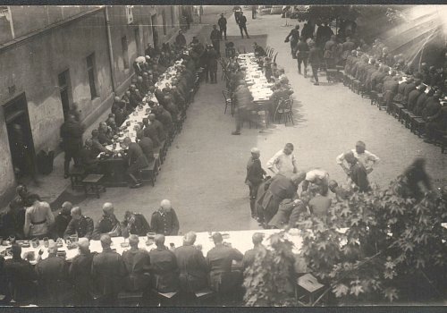 Wymiary: wysokość - 9 cm, szerokość - 14 cm; Materiał: papier fotograficzny; Technika: fotograficzna; Pochodzenie: Żory, G&oacute;rny Śląsk; Datowanie: lata 1922-1939; Autor: brak danych 
Fotografia czarno-biała przedstawiająca żołnierzy (II Dywizjonu 23 Pułku Artylerii Lekkiej w Żorach) podczas wsp&oacute;lnego posiłku na placu koszarowym. Fotografia wykonana z ptasiej perspektywy, na kt&oacute;rej widać cztery długie stoły i fragment zabudowań koszarowych (po lewej).