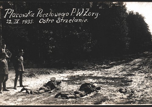 Wymiary: wysokość - 8,7 cm, szerokość - 13,5 cm; Materiał: papier fotograficzny; Technika: fotograficzna; Pochodzenie: Żory, G&oacute;rny Śląsk; Datowanie: 22 IX 1935 r.; Autor: brak danych 
Fotografia czarno-biała przedstawiająca żorskich listonoszy i żołnierzy w trakcie ćwiczeń strzeleckich w ramach przysposobienia wojskowego. Na fotografii uwieczniono dw&oacute;ch listonoszy strzelających do celu w pozycji leżącej. Obok nich strzelanie obserwuje dw&oacute;ch wojskowych i jeden mężczyzna w ubraniu cywilnym (garnitur). W prawym g&oacute;rnym rogu napis:&nbsp;Plac&oacute;wka Pocztowego P.W. Żory 22 IX 1935. Ostre Strzelanie. Na rewersie odręczny napis długopisem:&nbsp;Marciniec.